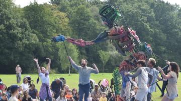 Puppeteers controlling a 13 foot metal puppet in a park while audiences look on