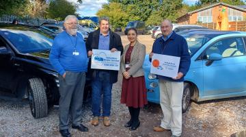Three men and one woman holding signs representing the two organisations behind the community transport partnership
