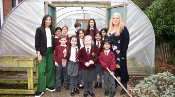 Oak Cottage Primary School's Eco-committee outside their polytunnel, with Let's Go Zero Climate Action Advisor Kumari Kher (left) and the school's sustainability lead Jane Newman (right)