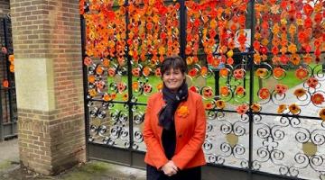 councillor grinsell stands at the gates of brueton park which are decorated with crochet flowers in honour of the 16 days campaign