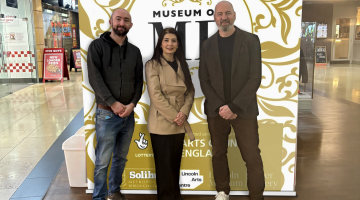 Two men and one woman stand in front of a sign in Touchwood advertising Museum of Me
