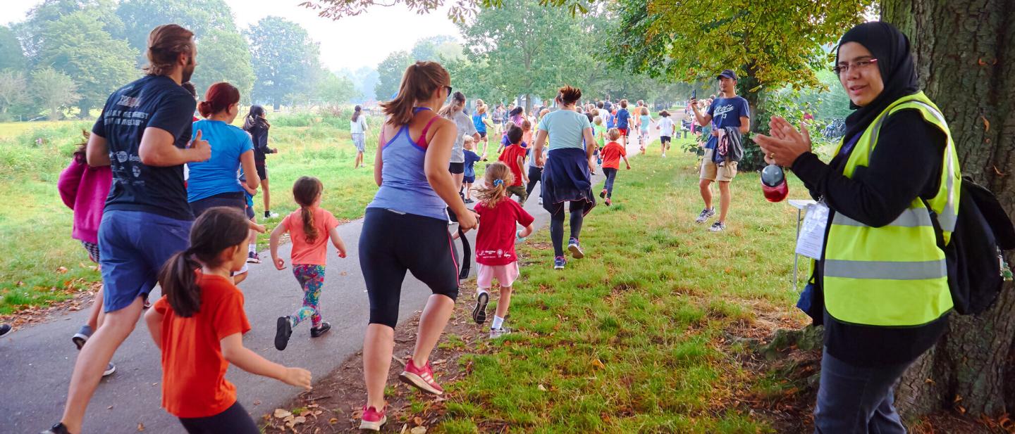 Families running in park while a spectator claps