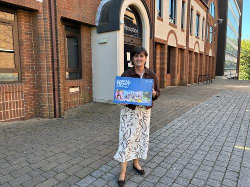 karen grinsell outside of the council house holding an annual report poster